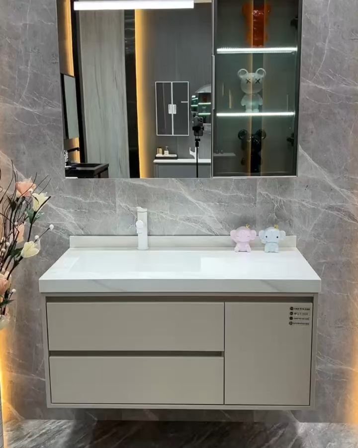 Taupe bathroom vanity with a white countertop and large illuminated mirror against marble walls.