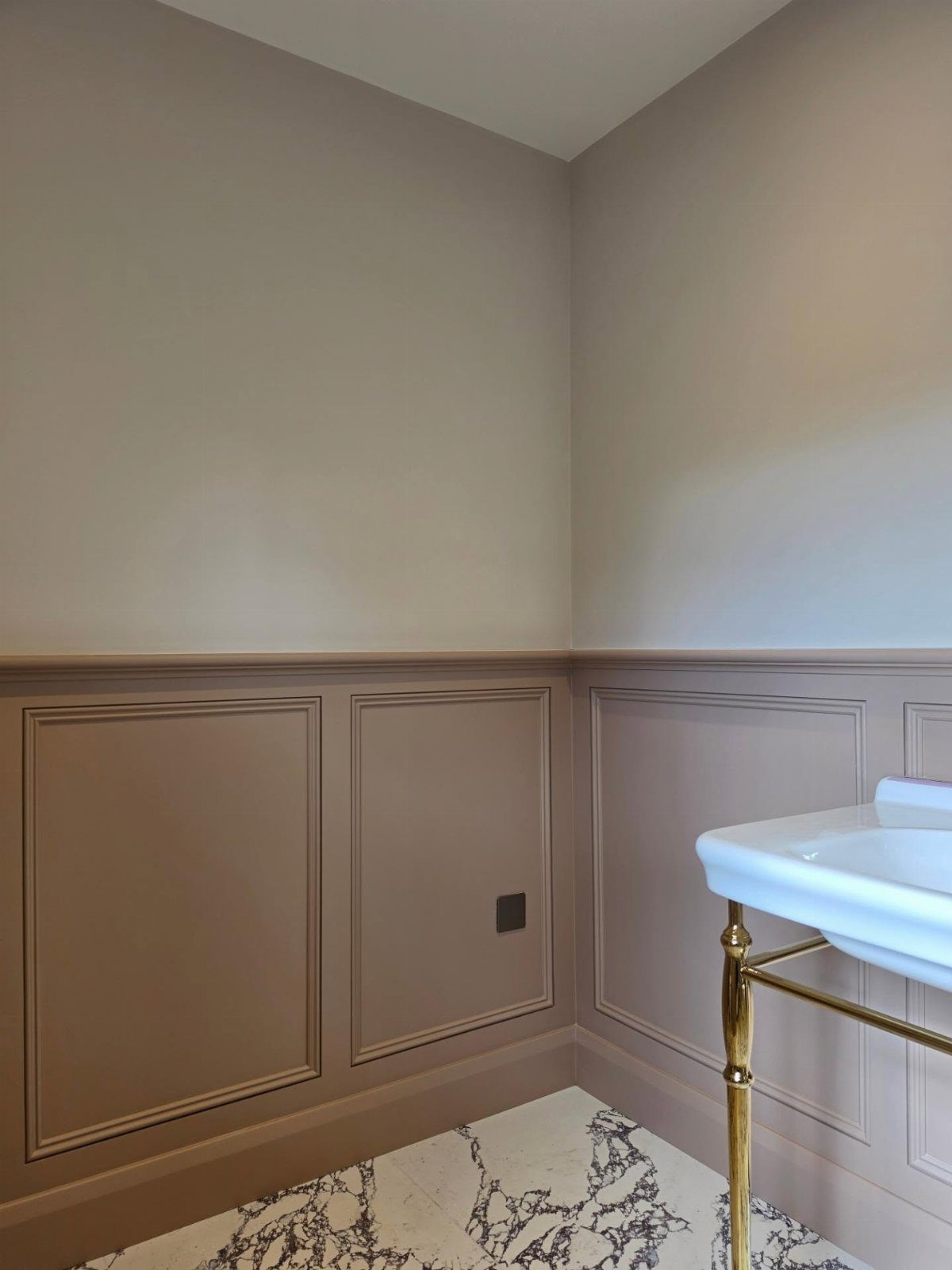 Taupe wainscoting and painted walls in a bathroom with marble flooring and a white sink.