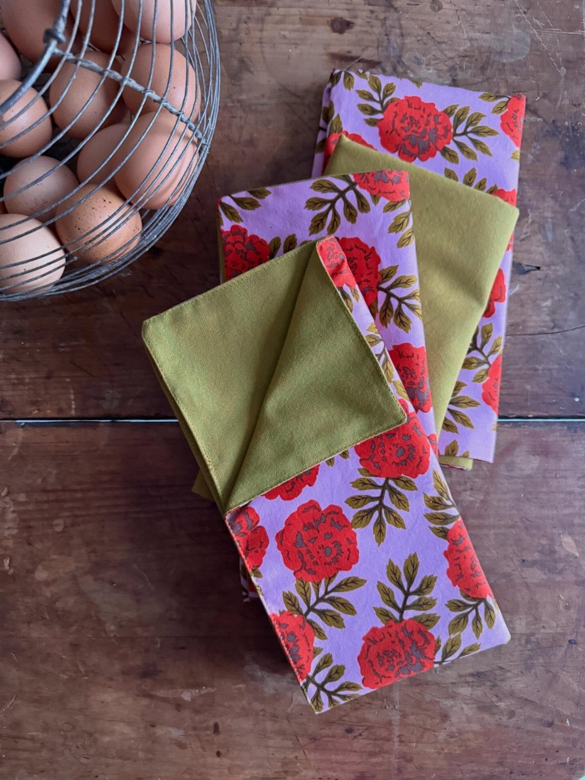 Folded floral and olive green cloth napkins resting on a rustic wooden table.