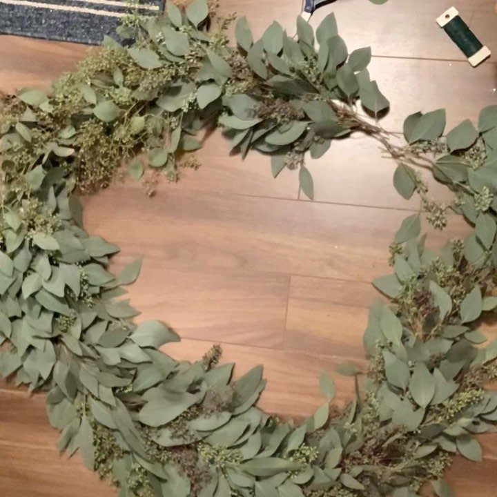 Eucalyptus leaves and dried floral sprigs arranged in a circular wreath on a wooden floor.