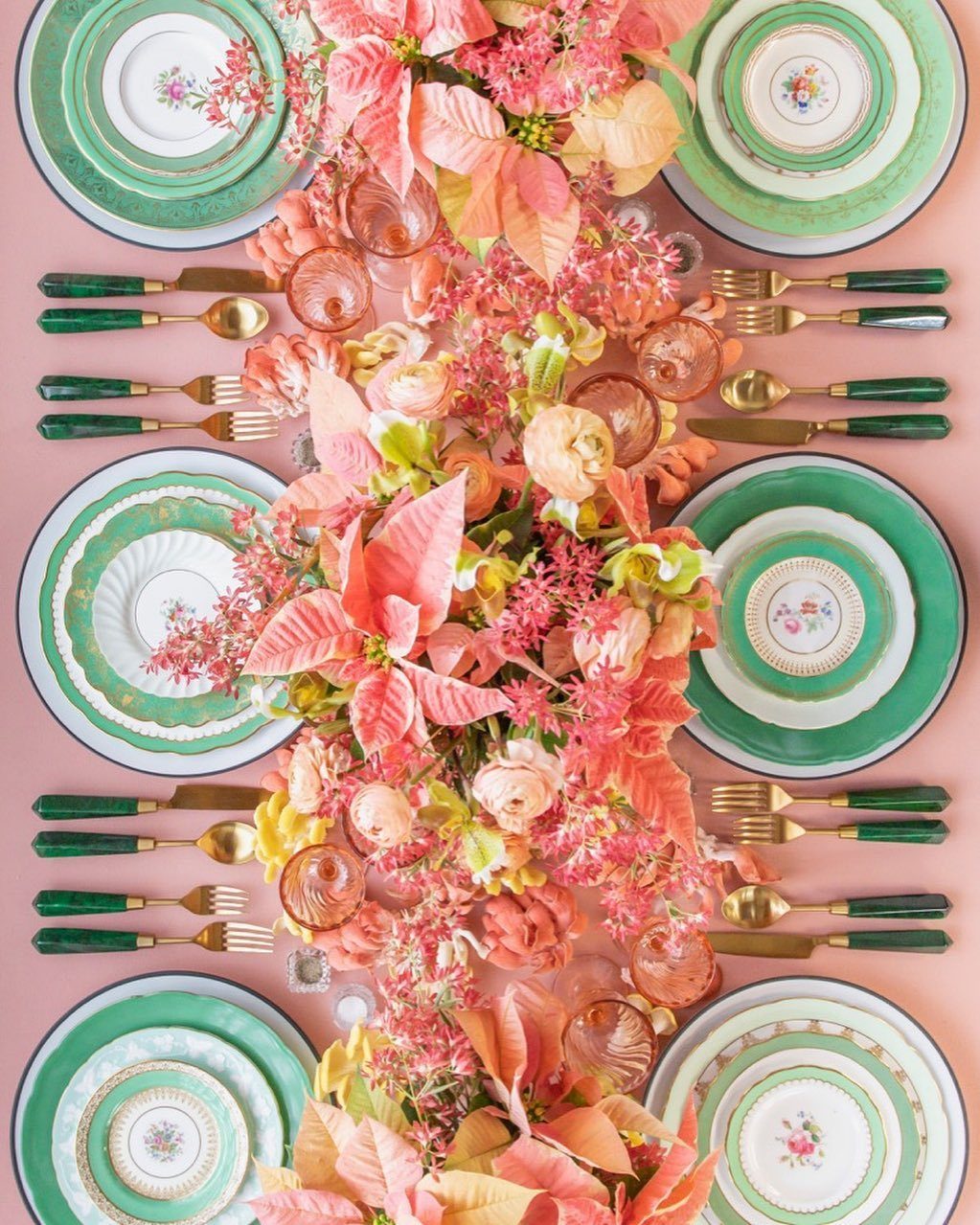 Top-down view of a decorated table with green plates, gold flatware, and pink floral centerpiece.
