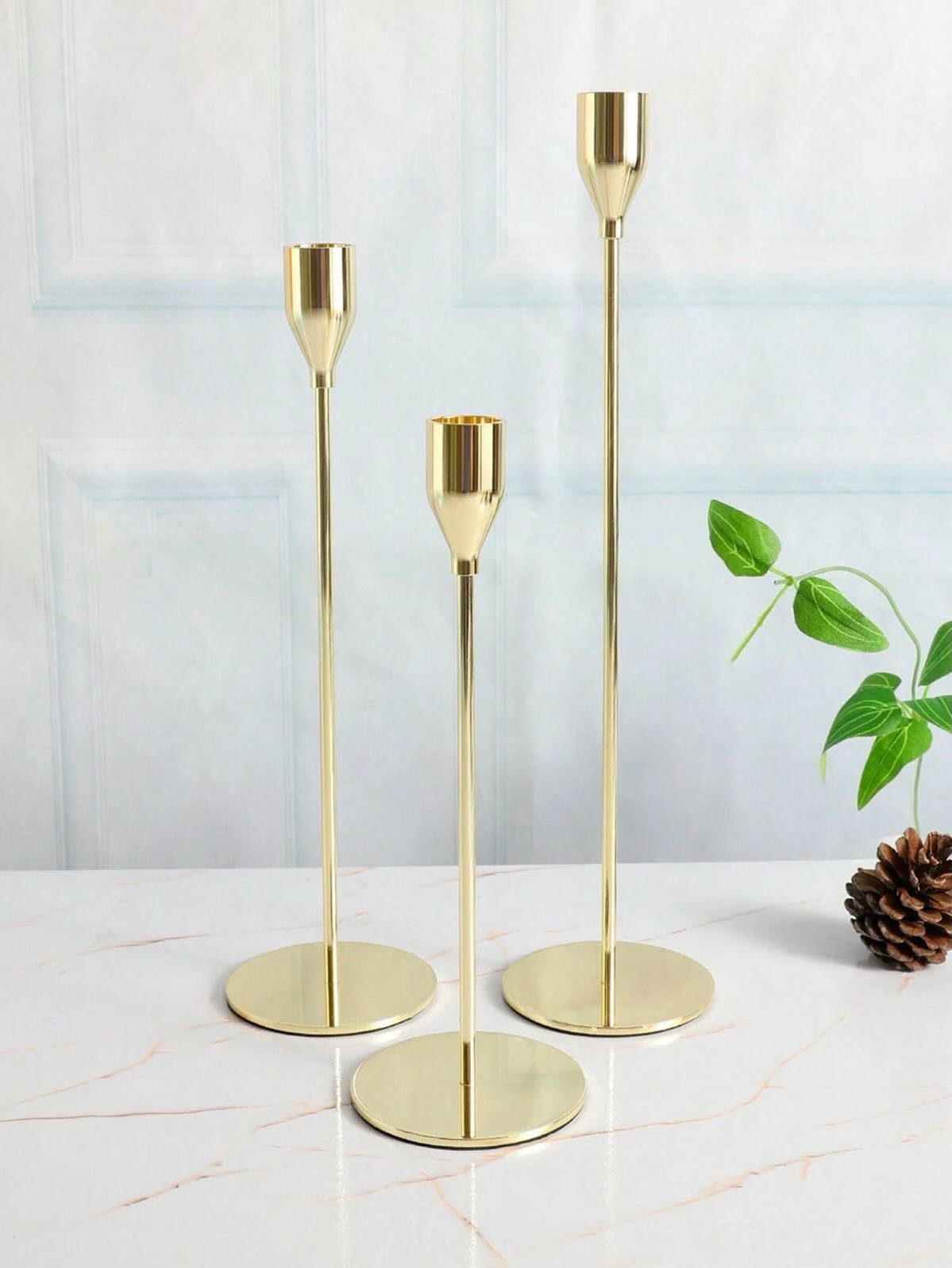 Three gold metal candle holders of different heights on a white marble tabletop.