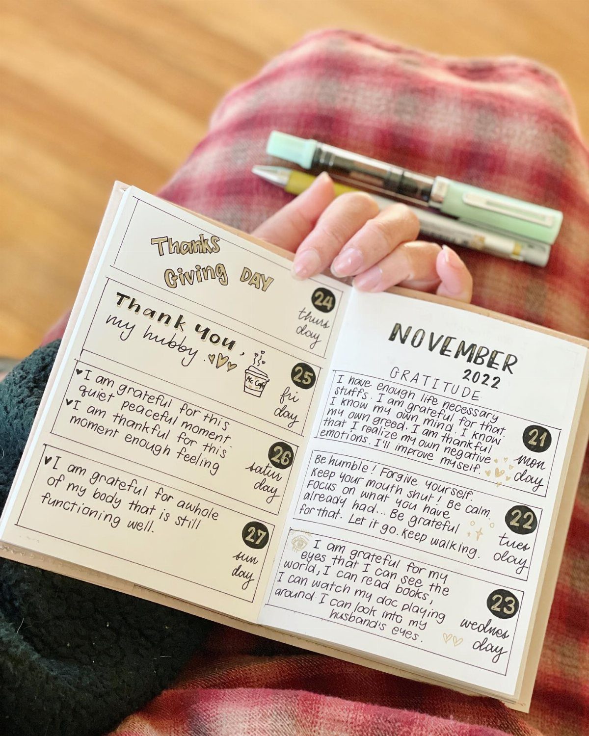 Hands holding an open notebook filled with handwritten gratitude entries and pens.