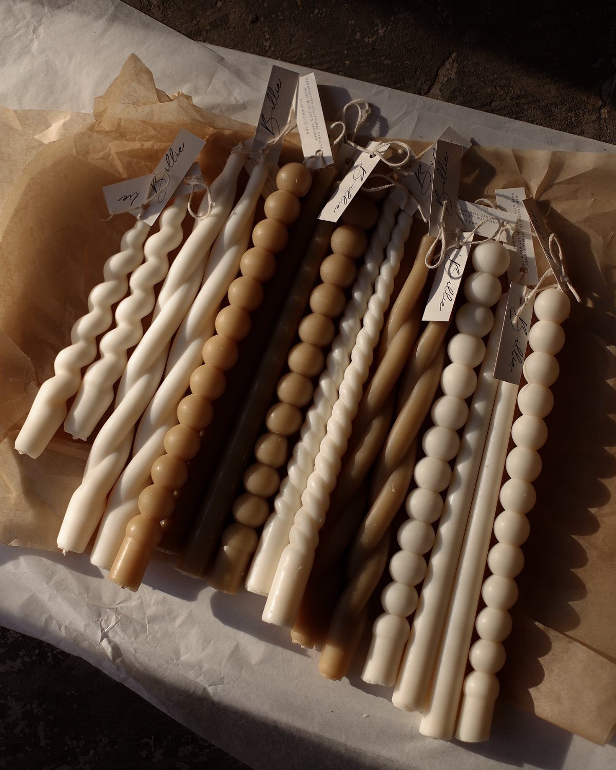 Various cream and tan textured taper candles resting on brown parchment paper.