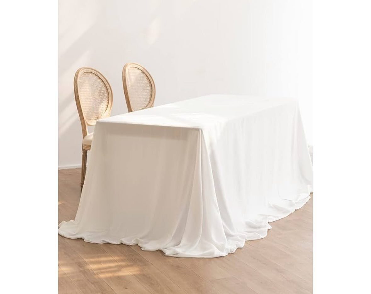 A white neutral tablecloth draped over a dining table with two cane back chairs.