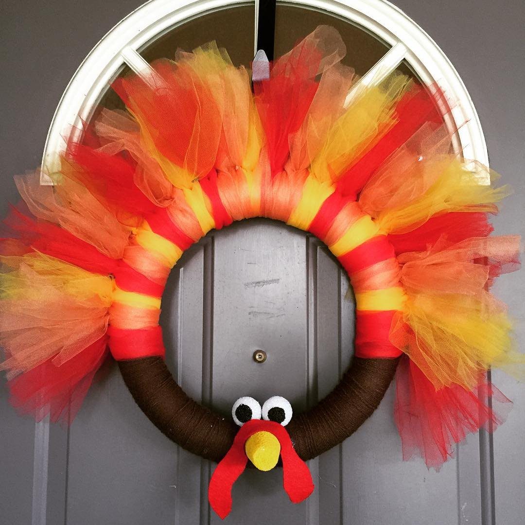 A turkey wreath made of brown fabric and colorful orange and yellow tulle feathers hanging on a door.
