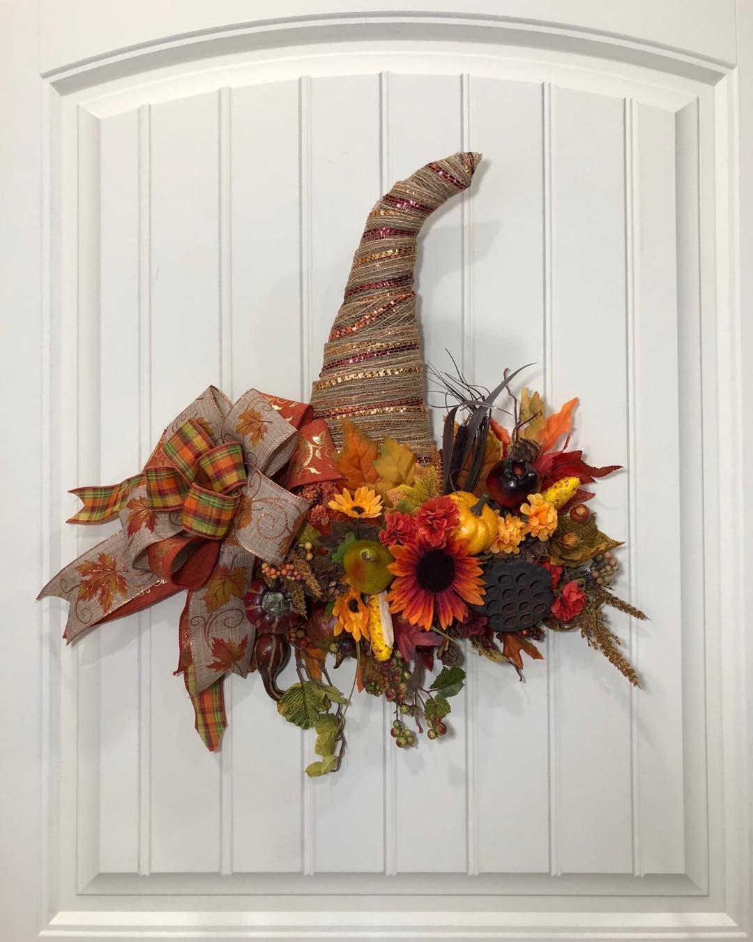 A cornucopia wreath with autumn leaves, pumpkins, and sunflowers hanging on a white door.