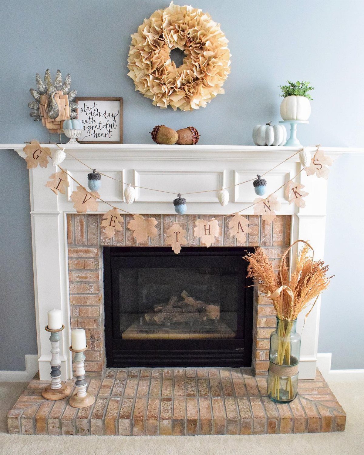 White fireplace mantel decorated with autumn leaves, a wreath, pumpkins, and a thankful garland.