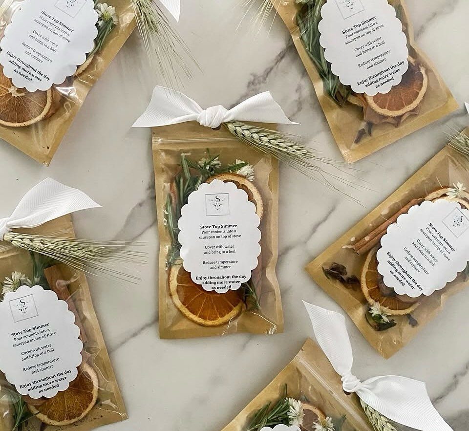 Small pouches containing dried orange slices, cinnamon, and greenery tied with white ribbons on marble.