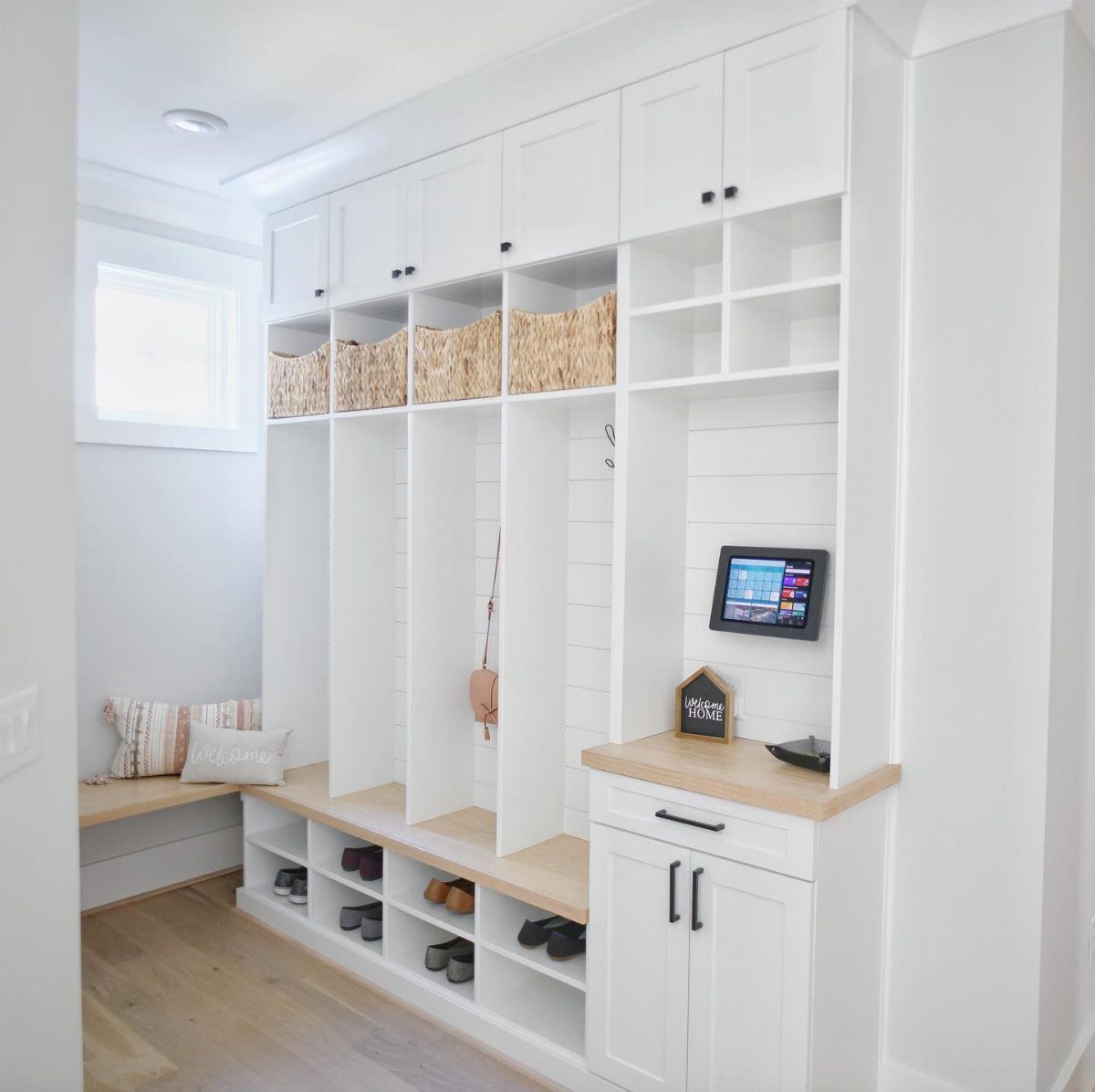 White built-in entryway organizer with wooden accents and storage cubbies in a bright hallway.