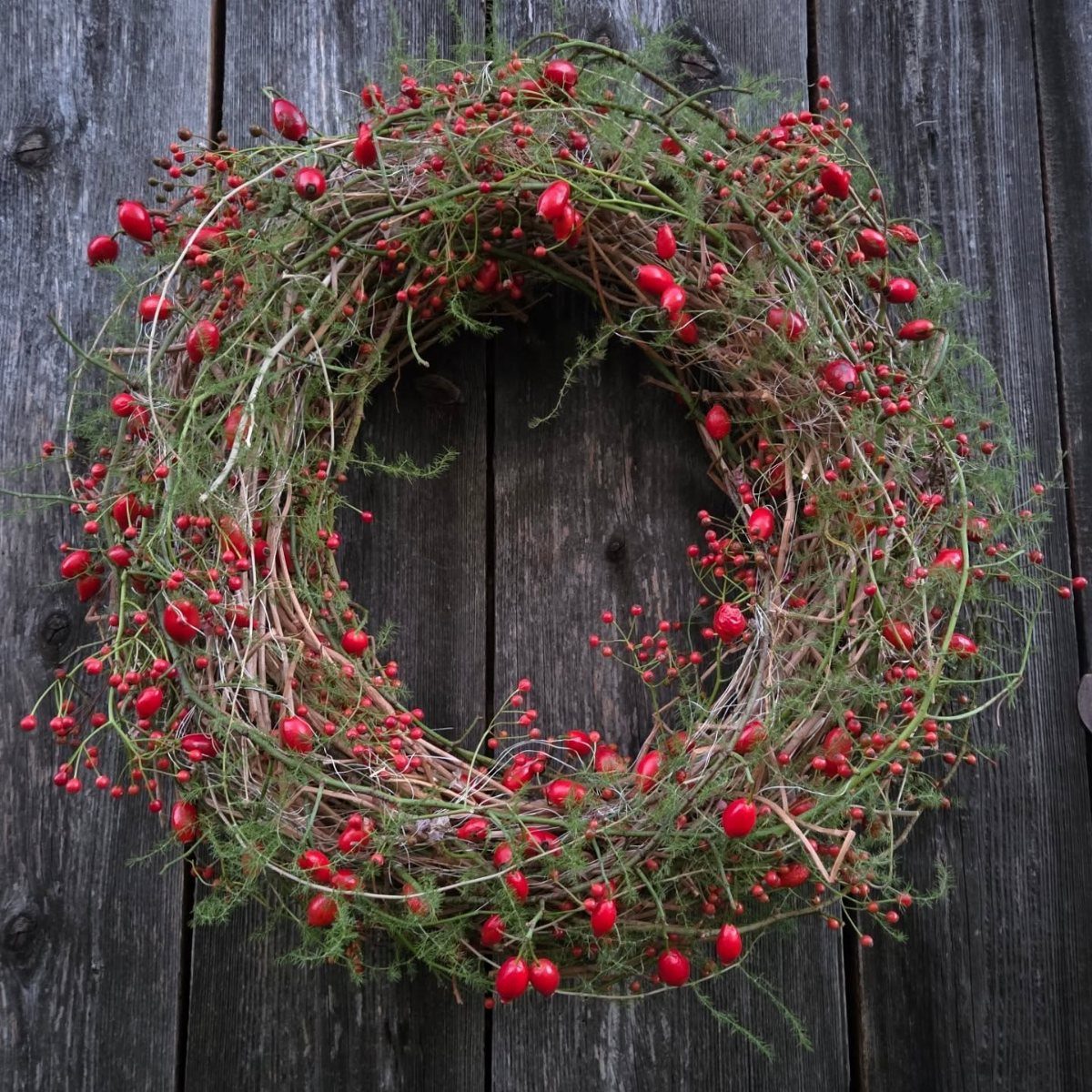 A festive wreath featuring green branches and vibrant red berries on dark wood.