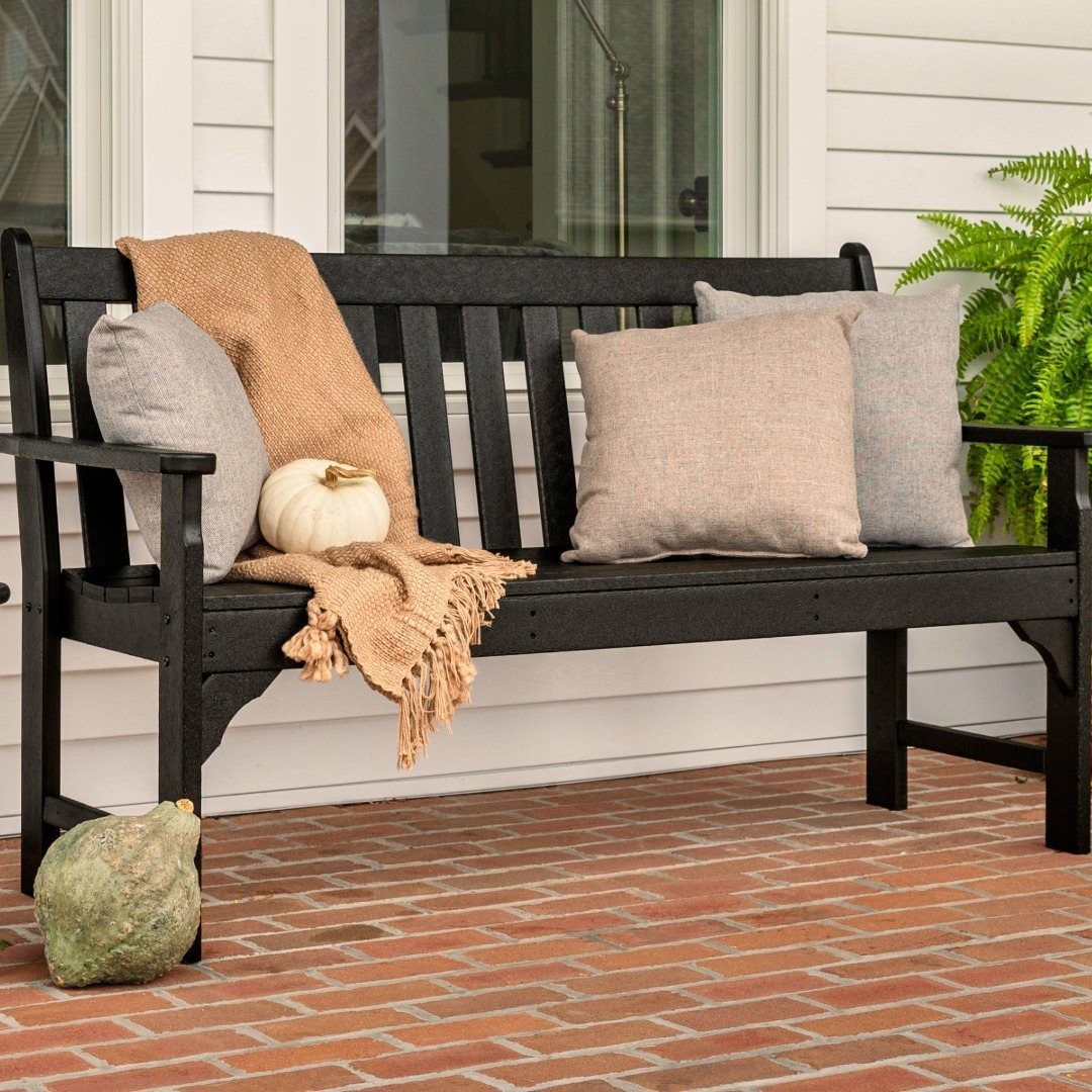 Black wooden bench decorated with grey pillows, a tan throw blanket, and a white pumpkin.