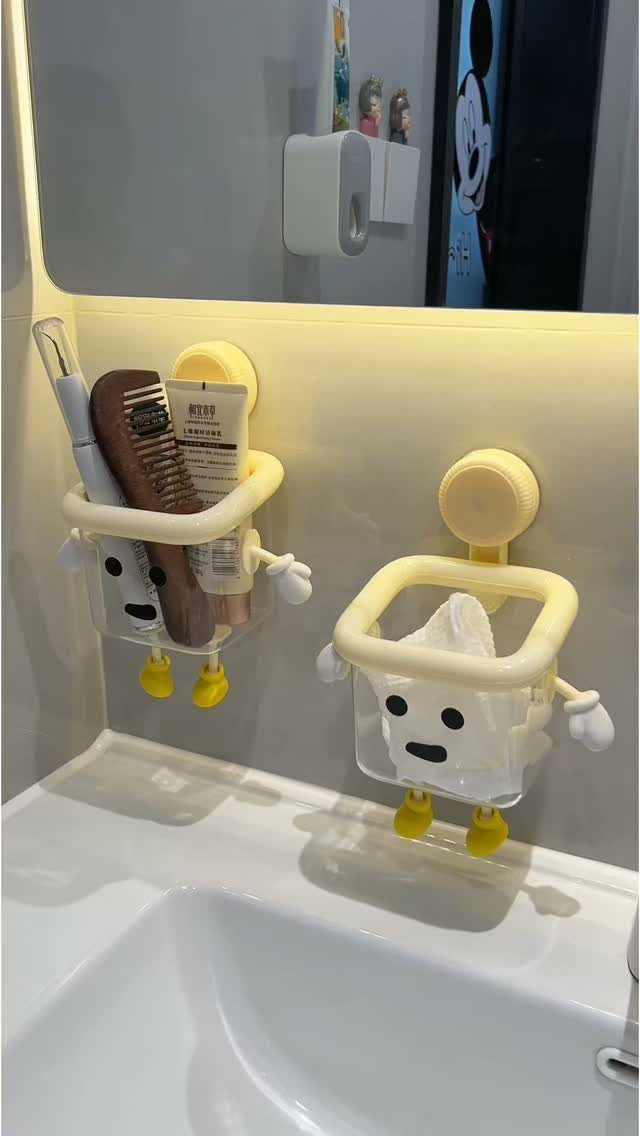 Character-shaped wall organizers holding a hairbrush and tissues above a white bathroom sink.