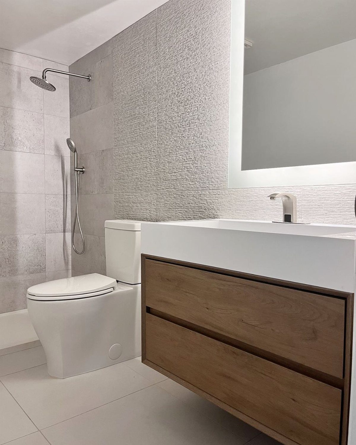 Wooden floating vanity with white sink next to a white toilet and tiled shower.