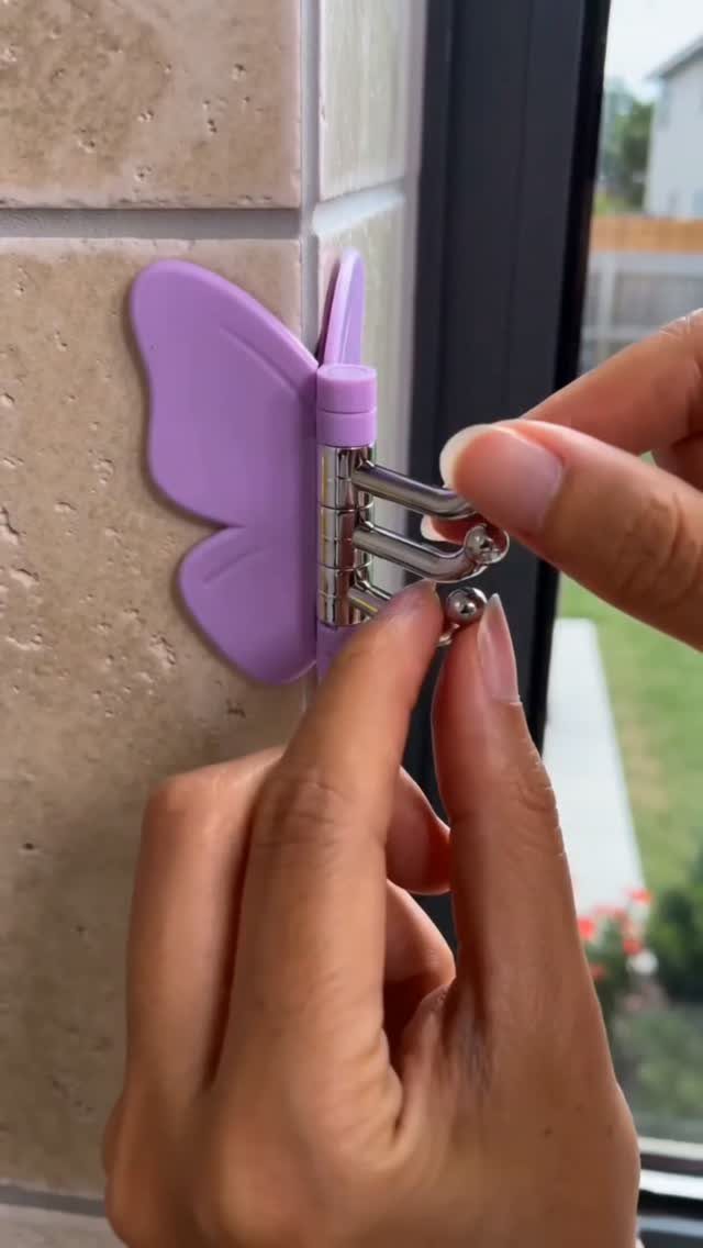 Hands demonstrating a purple butterfly-shaped hook mounted on a tiled wall.