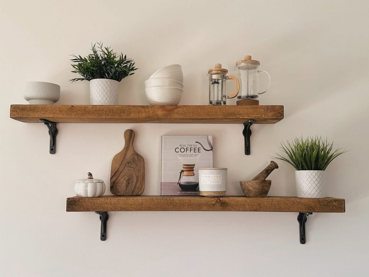 Two wooden floating shelves with black brackets holding plants, bowls, and coffee accessories.