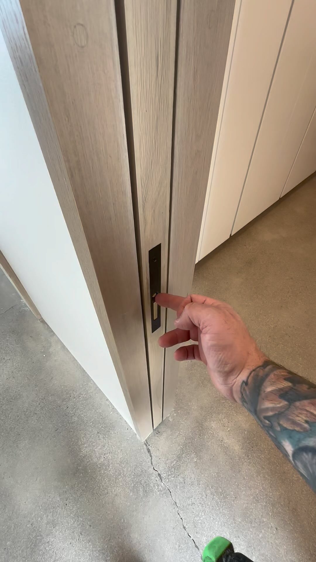 A hand reaching for a black handle on a light wood sliding door.