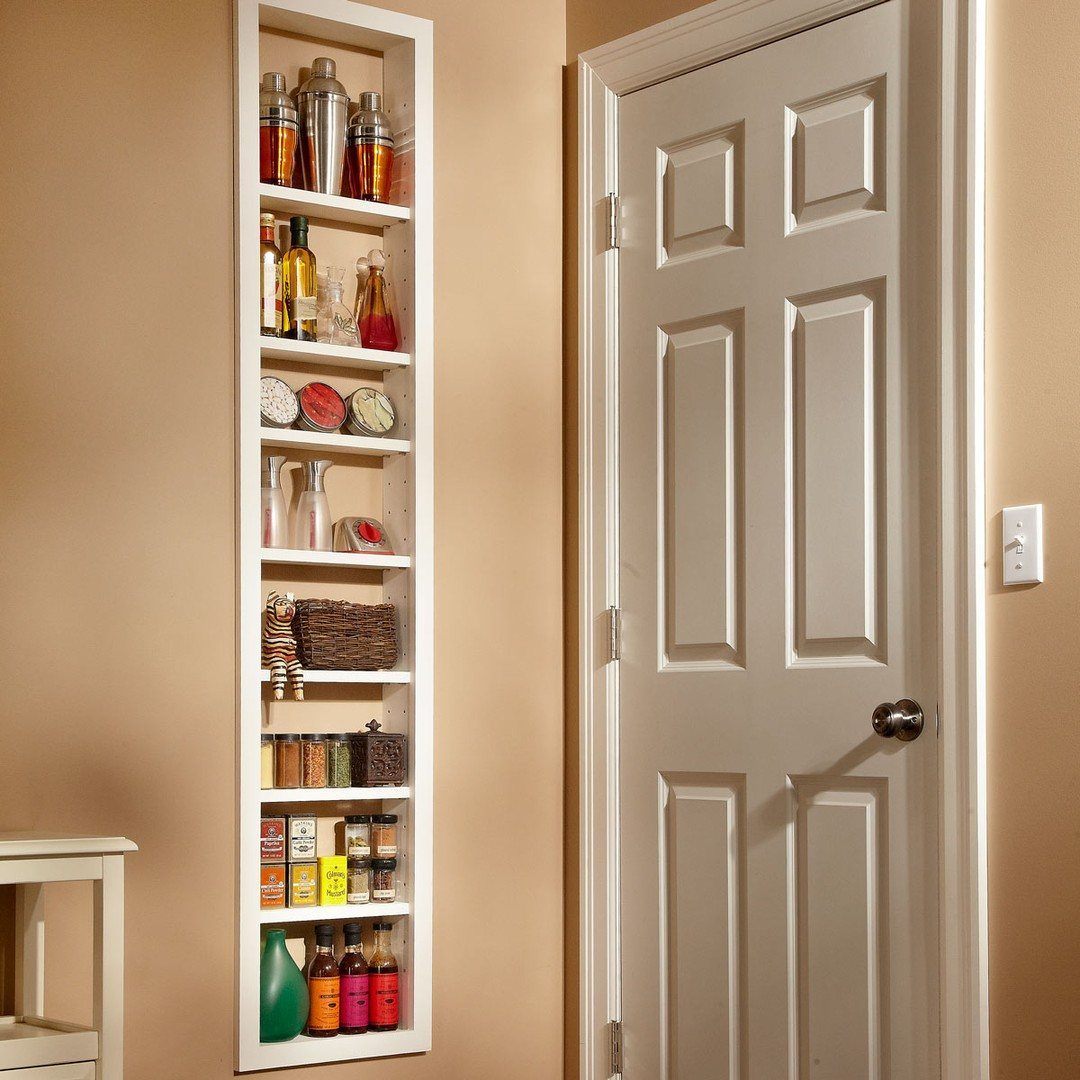 Tall white recessed shelving unit filled with various bottles and jars built into a beige wall.