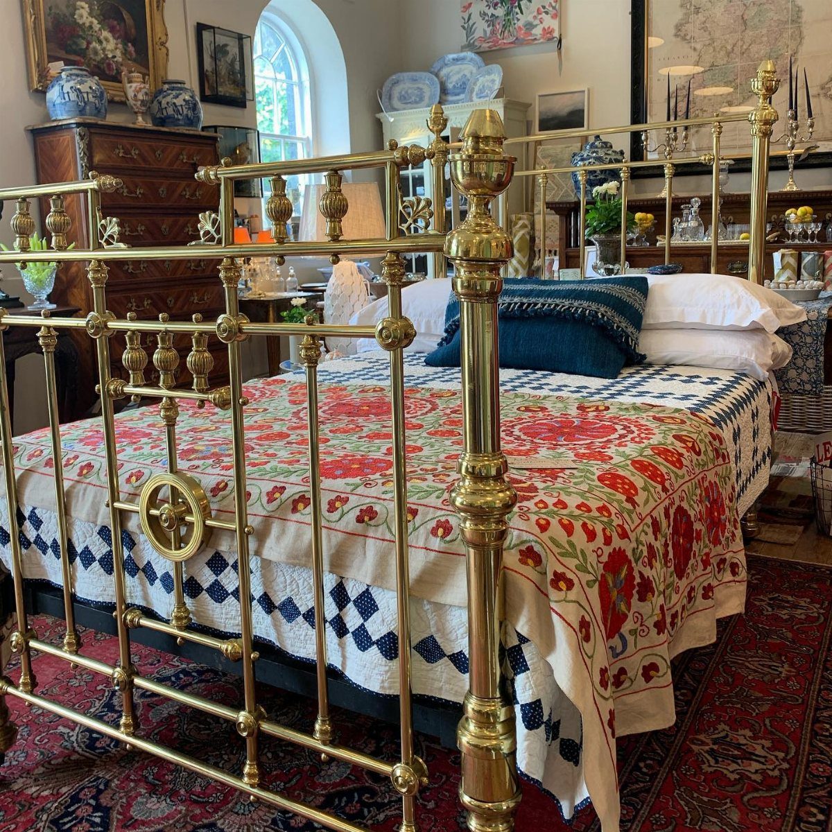 Antique brass bed with ornate gold metalwork and layered floral patterned linens in a bedroom.