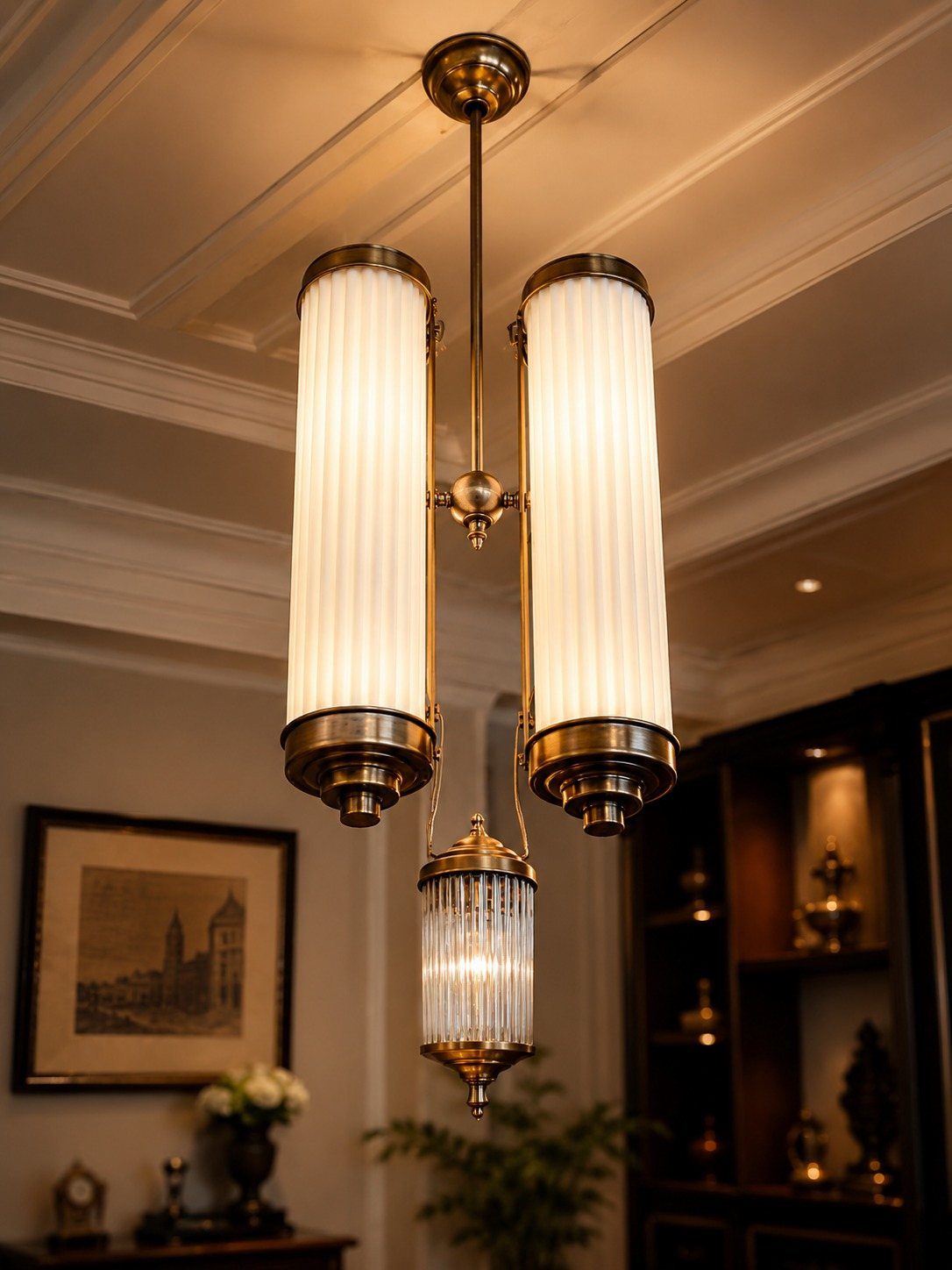 A brass chandelier with three ribbed white glass cylindrical shades hanging from a ceiling.