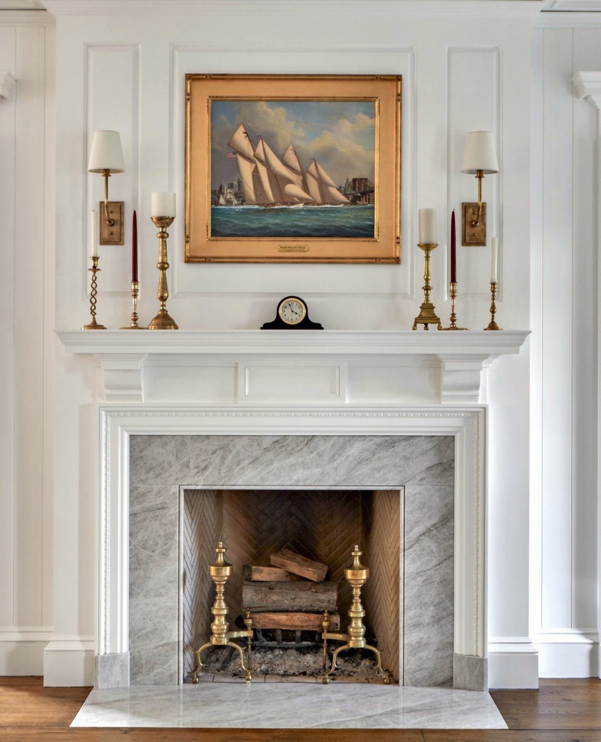 White marble fireplace with a styled mantel featuring brass candlesticks and a framed seascape painting.