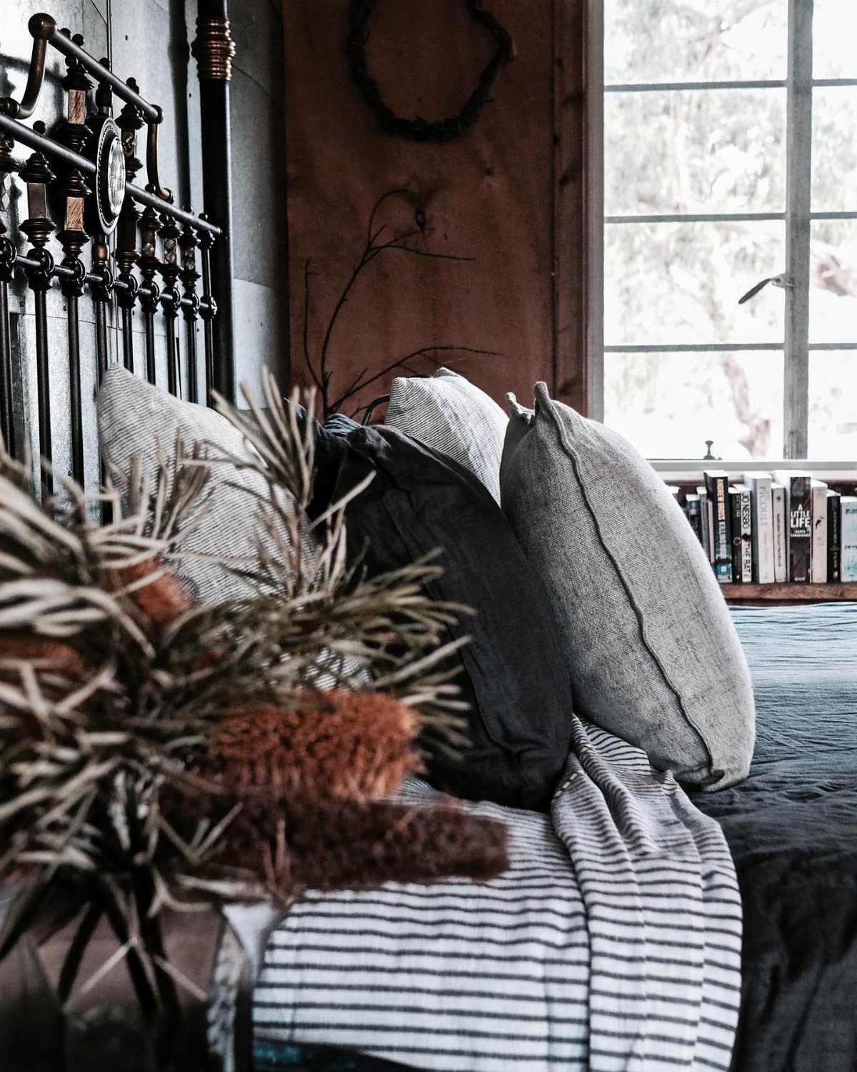 Ornate black cast iron headboard with grey linen pillows and striped bedding in a bedroom.
