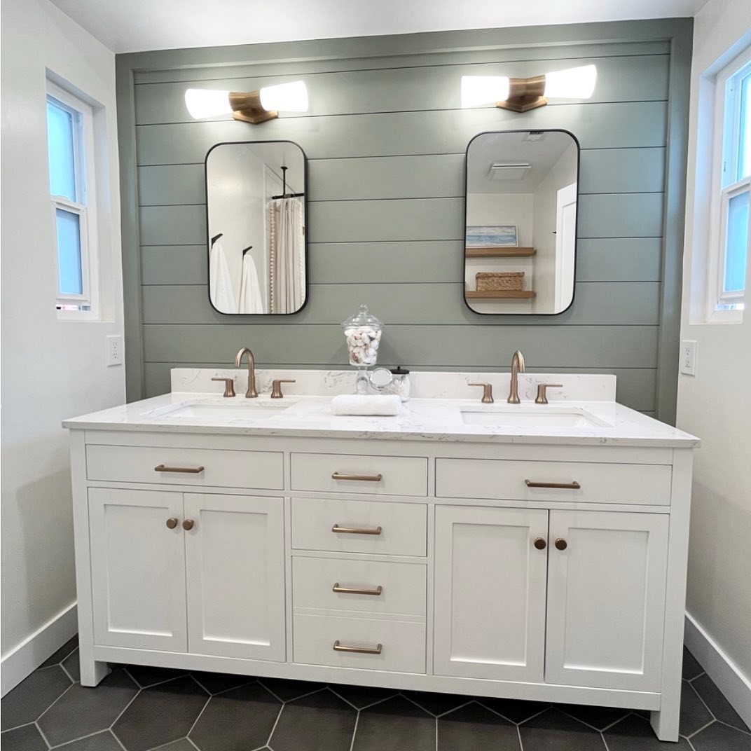 White double vanity with marble tops against a green shiplap accent wall and two mirrors.