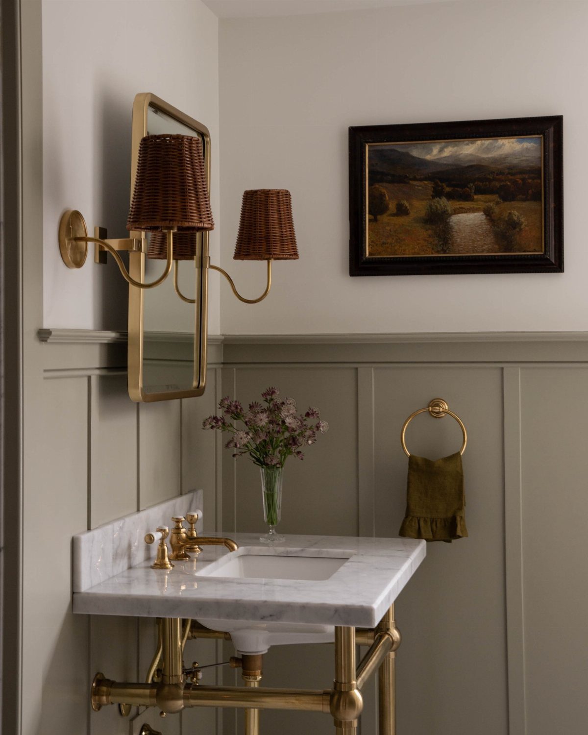 Gold metal sink fixtures and wicker wall sconces against gray paneled walls.