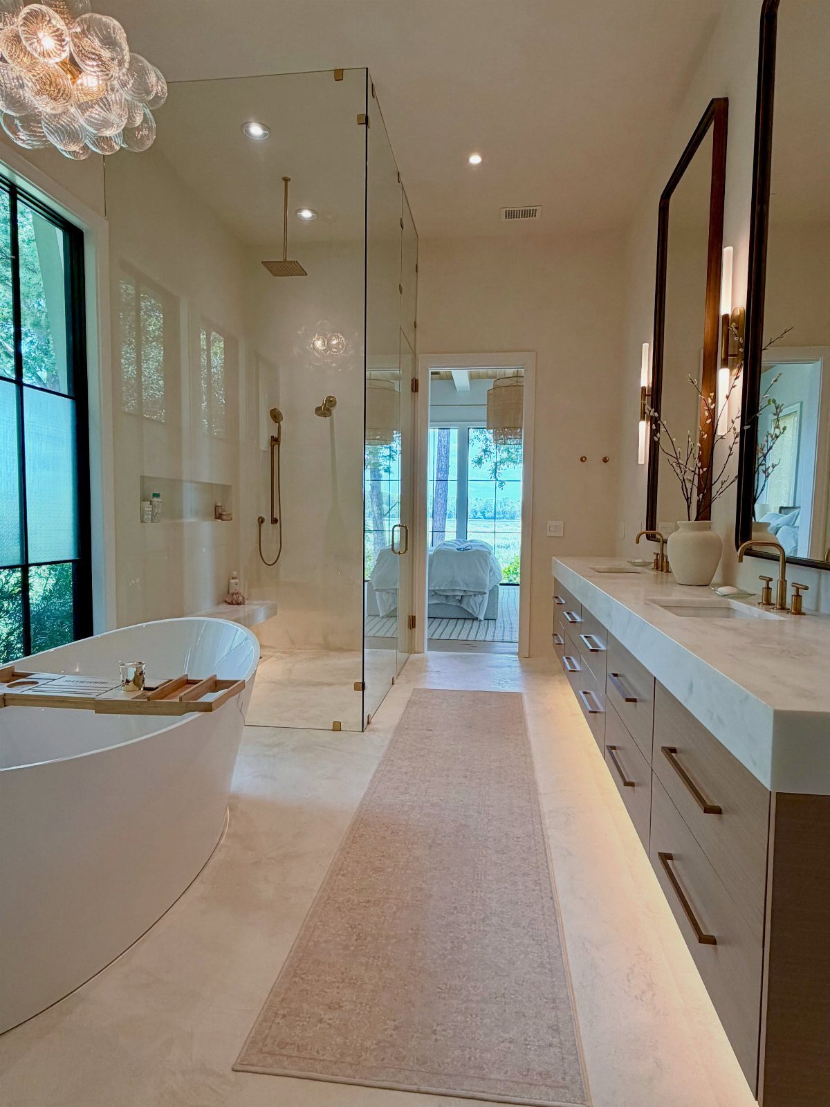 White freestanding tub in a luxury neutral bathroom with marble vanity and glass shower.
