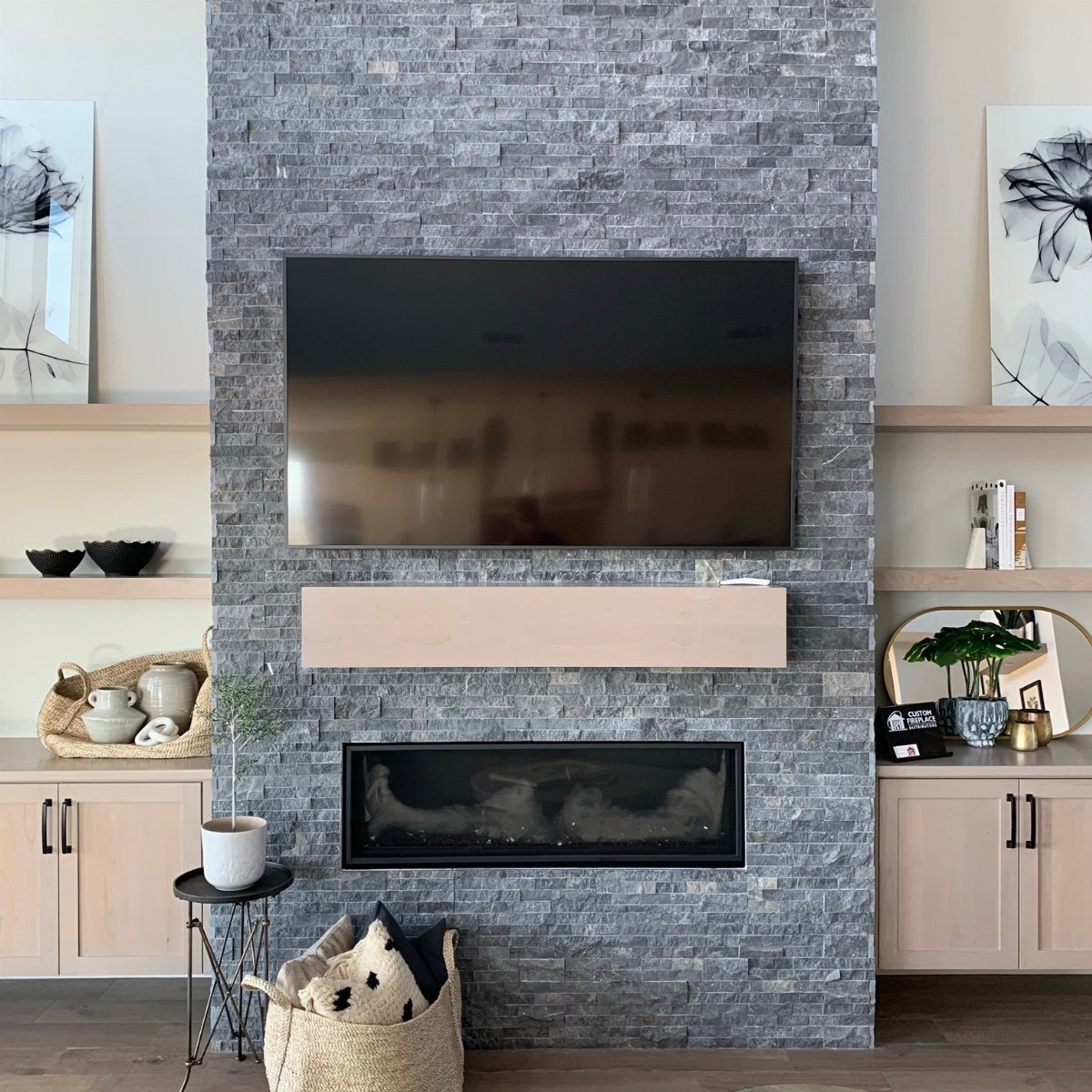 Grey stone stacked fireplace with a mounted television and light wood floating mantel.