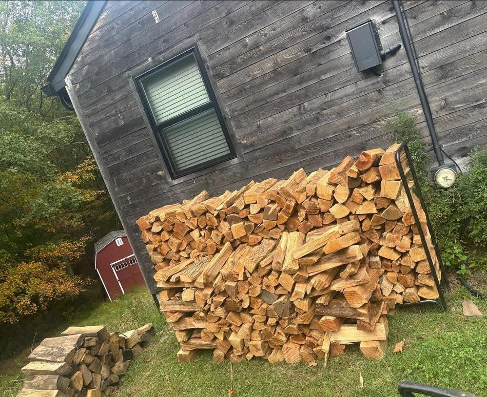 Stacked split firewood piled against the dark wooden exterior of a rustic building.