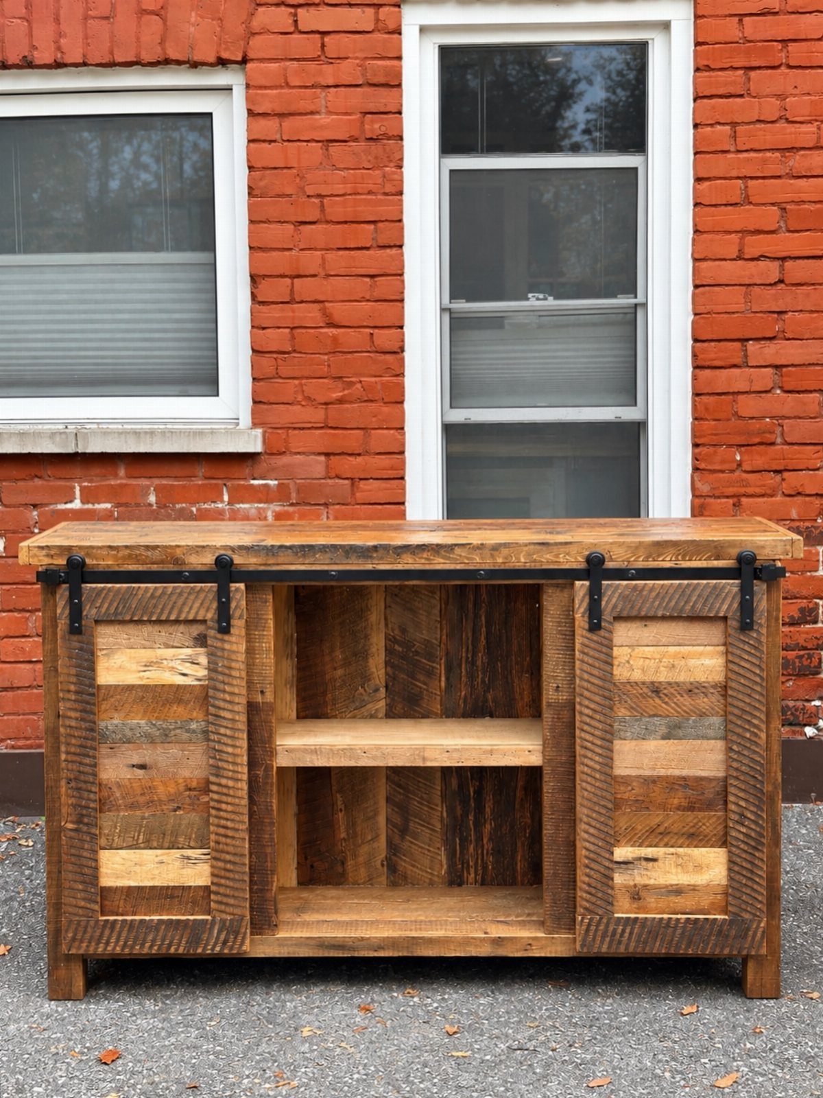 Reclaimed wood sideboard with sliding barn doors positioned against a red brick wall.