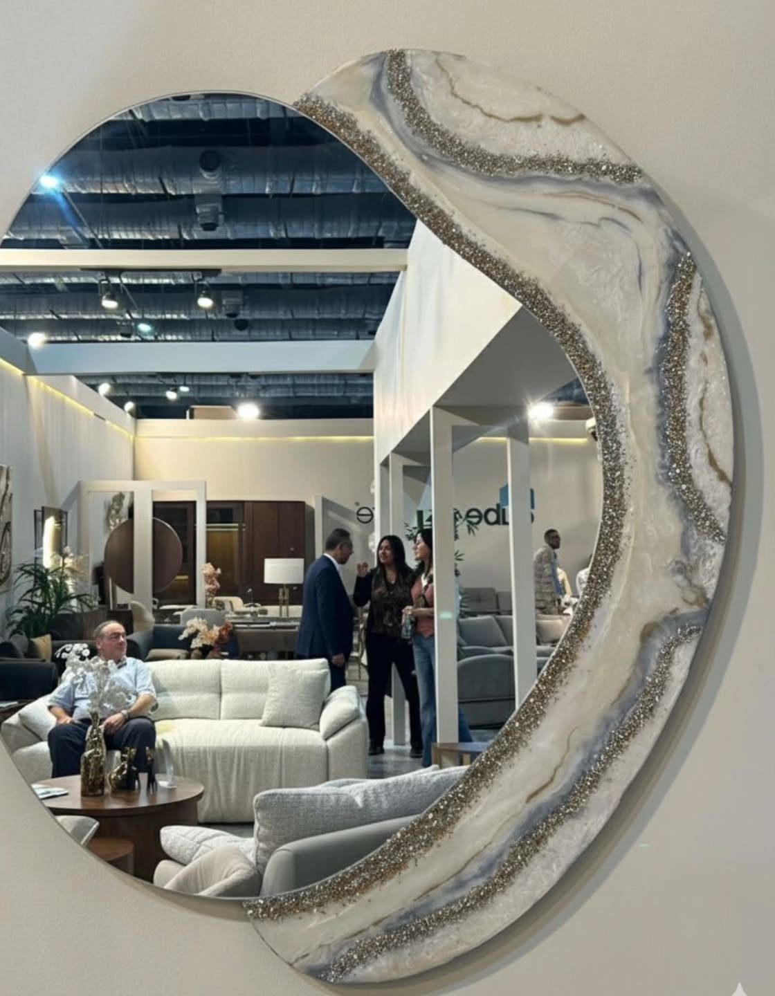 Large circular mirror with a decorative white and gold agate-style frame reflecting a furniture showroom.