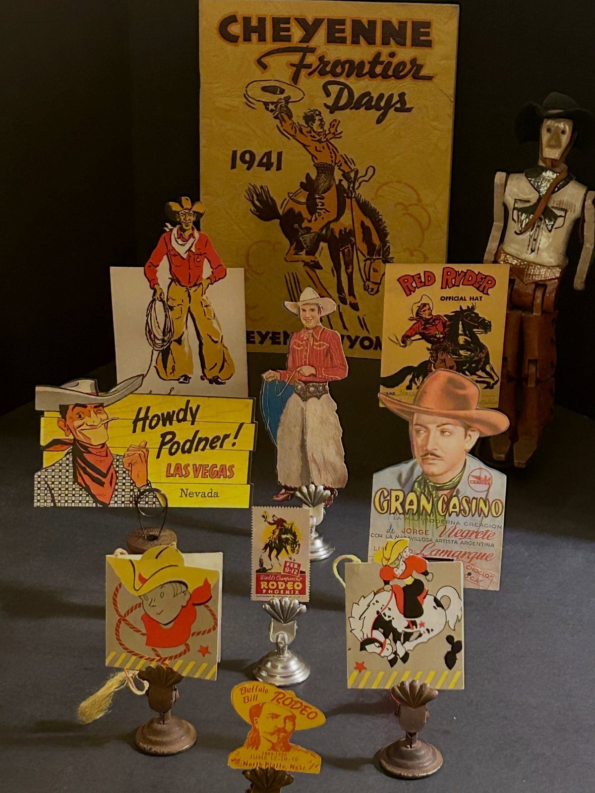Vintage rodeo posters and cowboy figurines arranged on a dark tabletop surface.