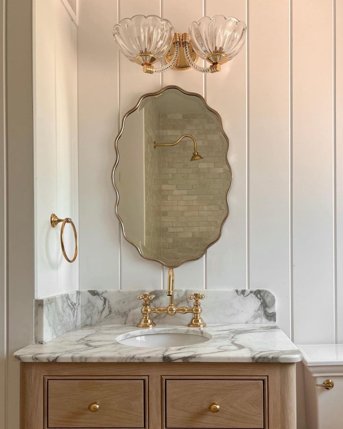 An ornate gold scalloped mirror hangs above a marble vanity with brass fixtures.