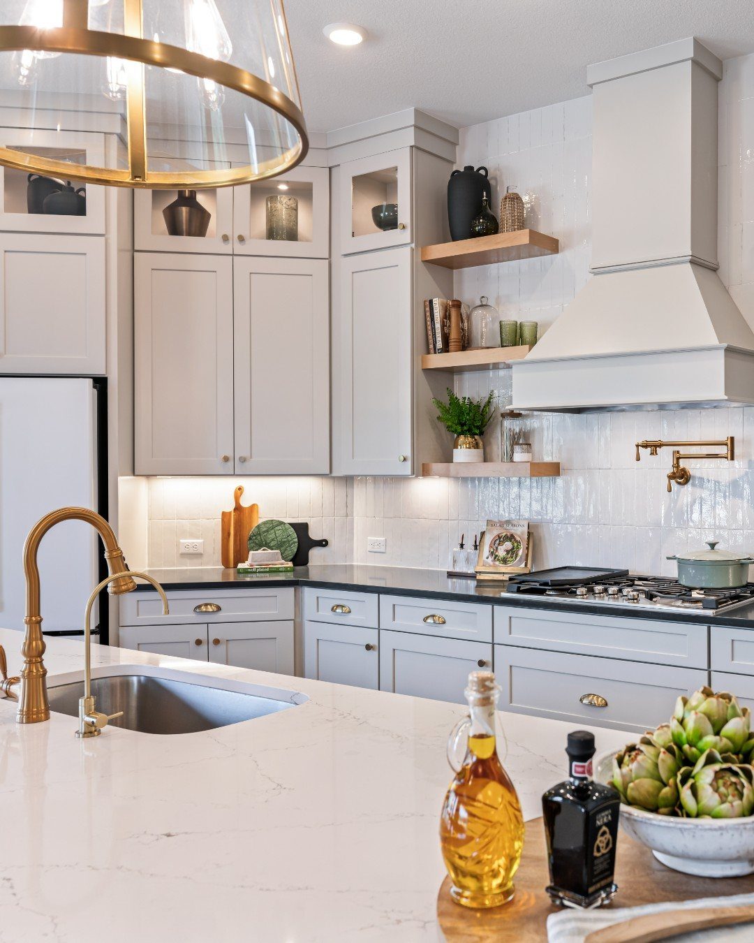 White kitchen with grey cabinets, black countertops, and a large gold pendant light hanging over the island.