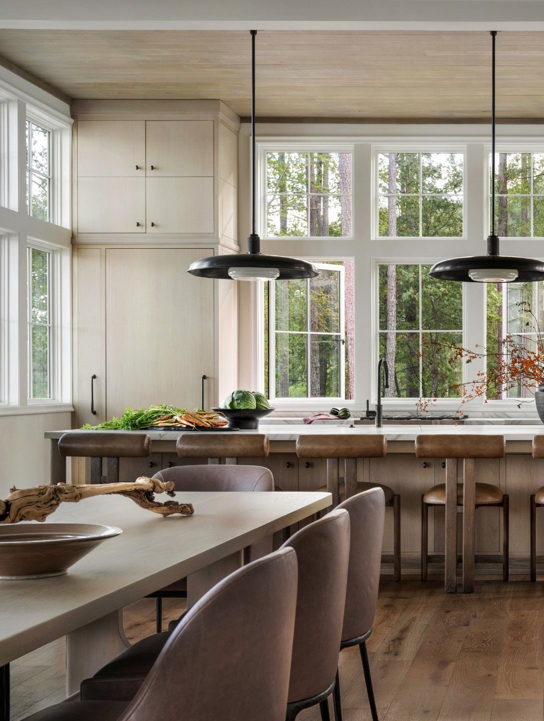Bright white kitchen with large windows overlooking green trees and black pendant lights.