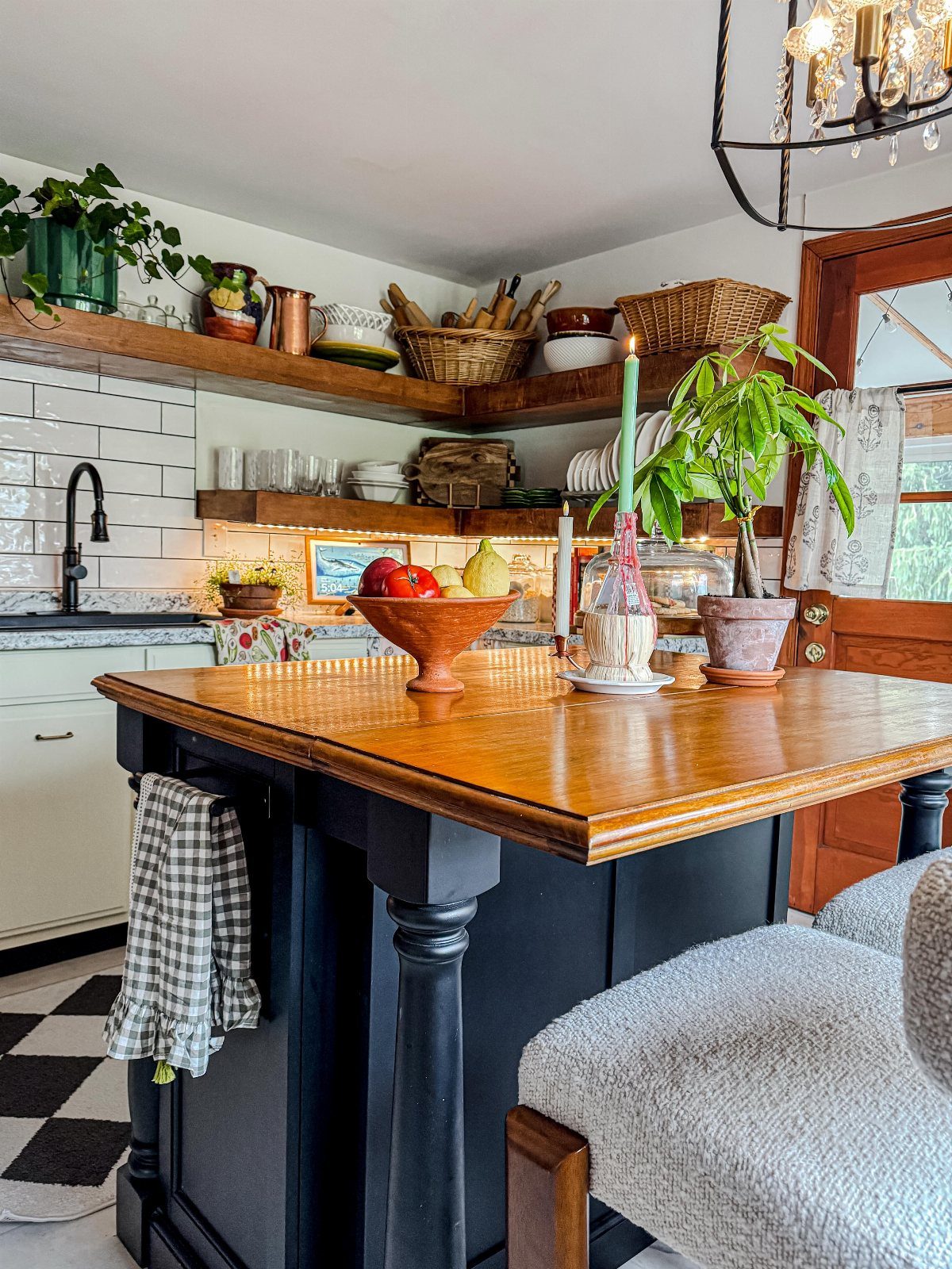 Wooden open shelves holding various kitchenware and plants above a white subway tile backsplash.