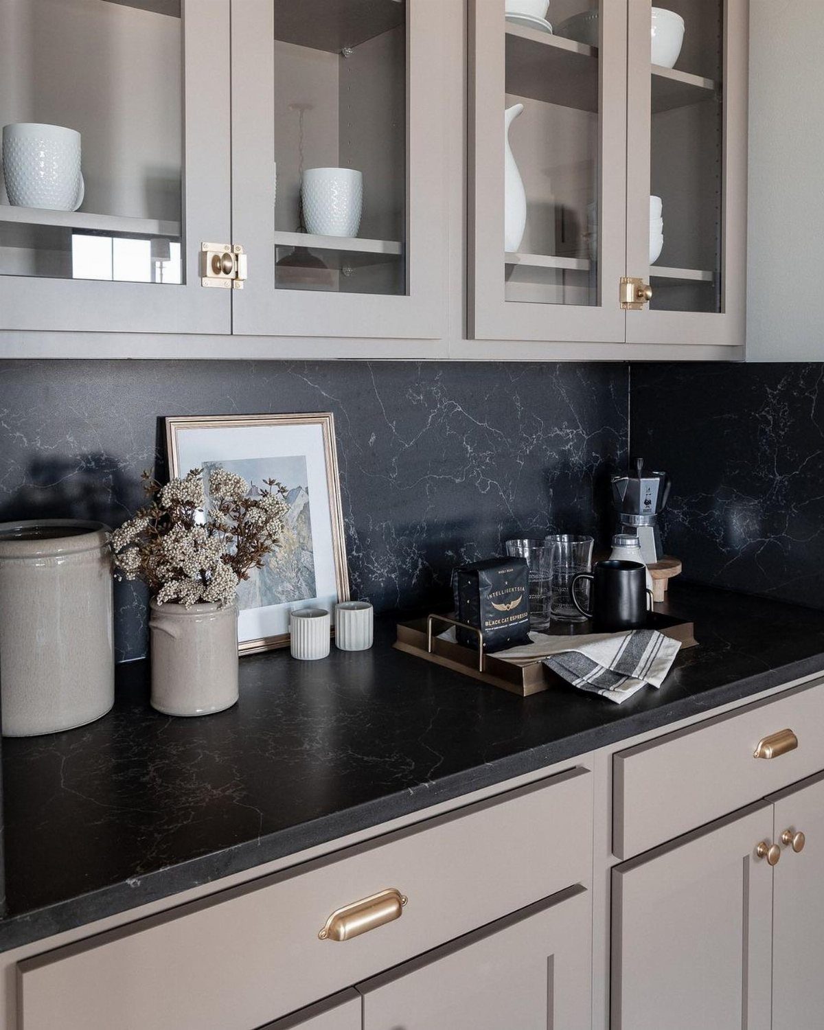 Black marble countertops with white veining paired with light grey kitchen cabinets and gold hardware.